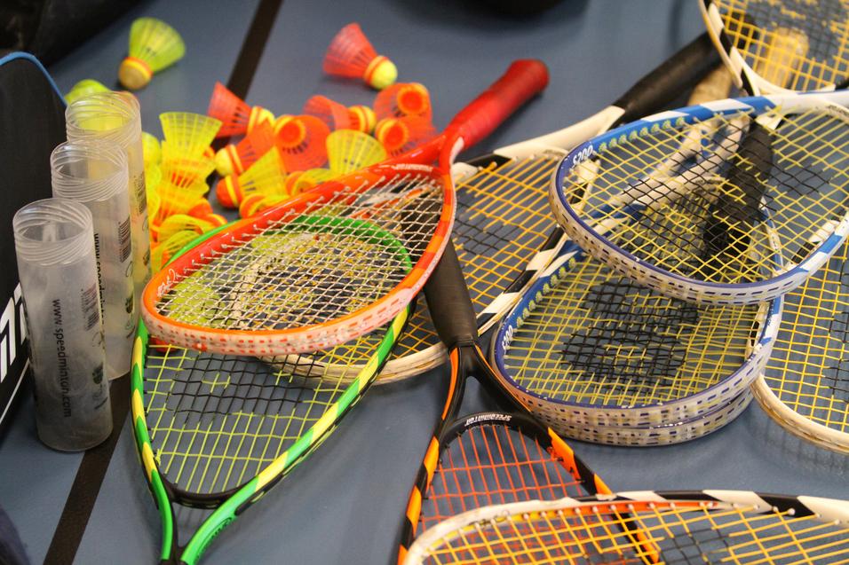 Bunte Badminton-Schläger und -Bälle liegen auf einem Tisch, umgeben von transparenten Schutzhüllen.