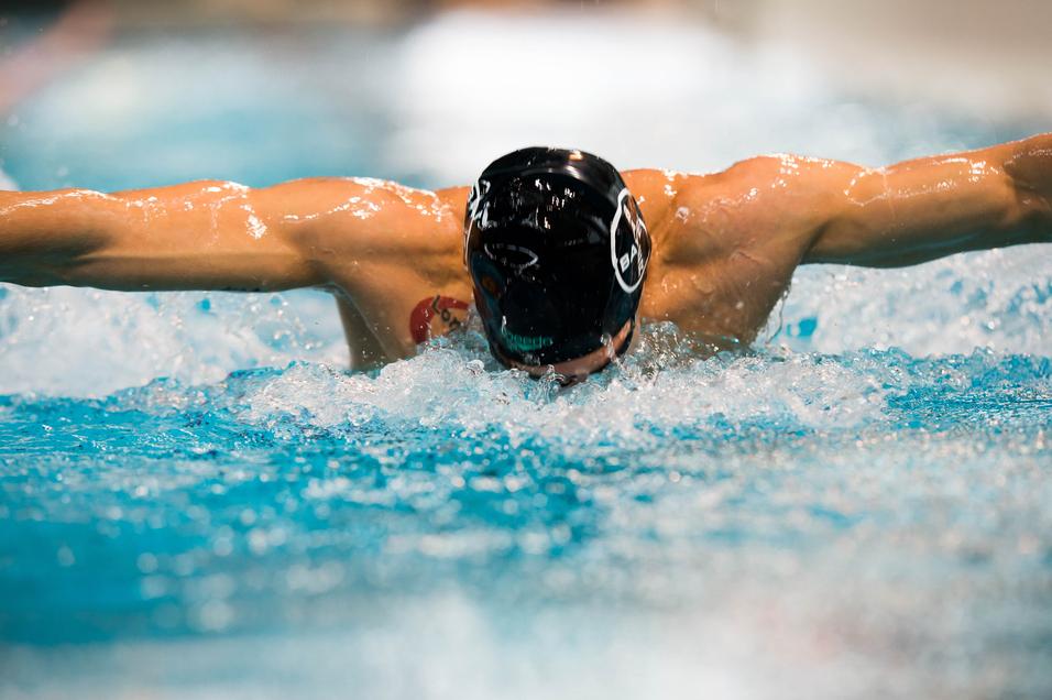 Schwimmer im Wasser führt einen Schmetterlingsschwimmzug aus, eine Hand nach vorne gestreckt, Wassertropfen spritzen.